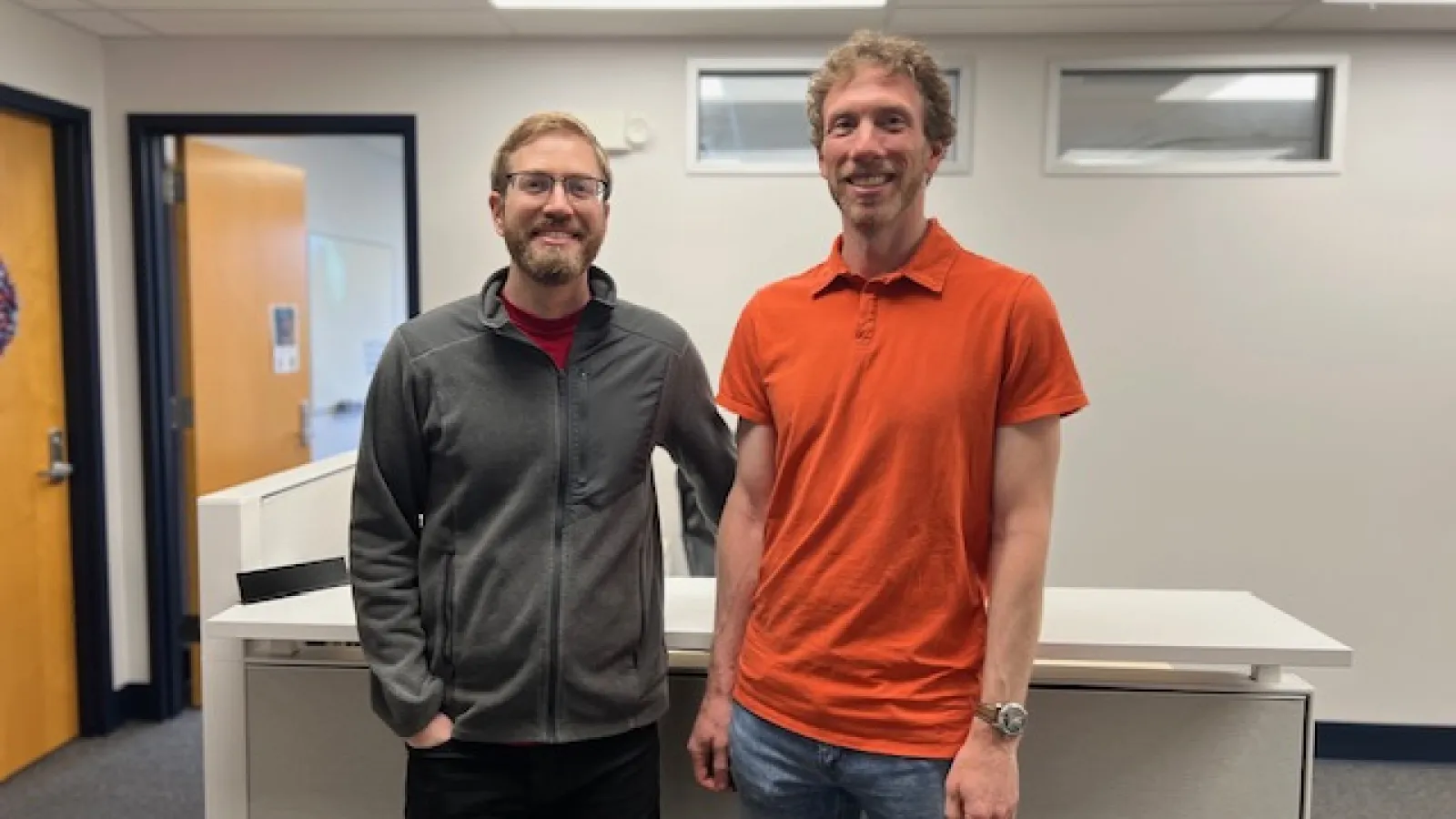 Tom and David standing together and smiling in front of a desk